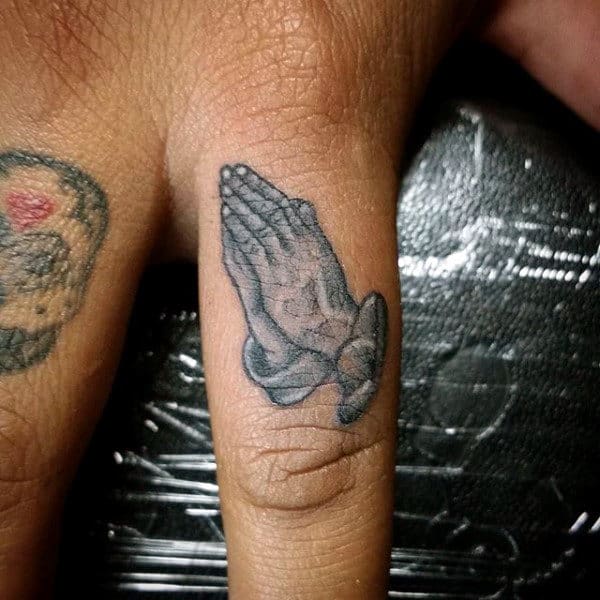 Tattoo of praying hands on a person's finger
