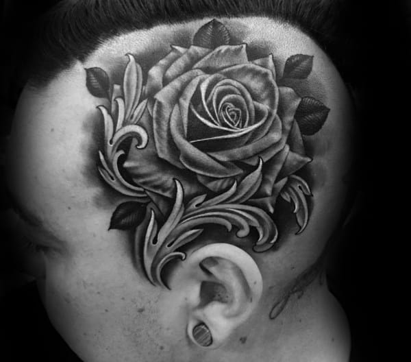 Black and white tattoo of a rose with leaves on the side of a man's head