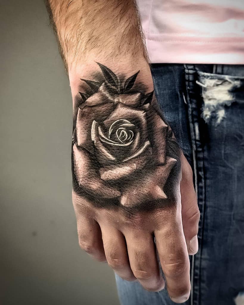 A stunning close-up of an intricately detailed black rose tattoo graces the back of a person's hand
