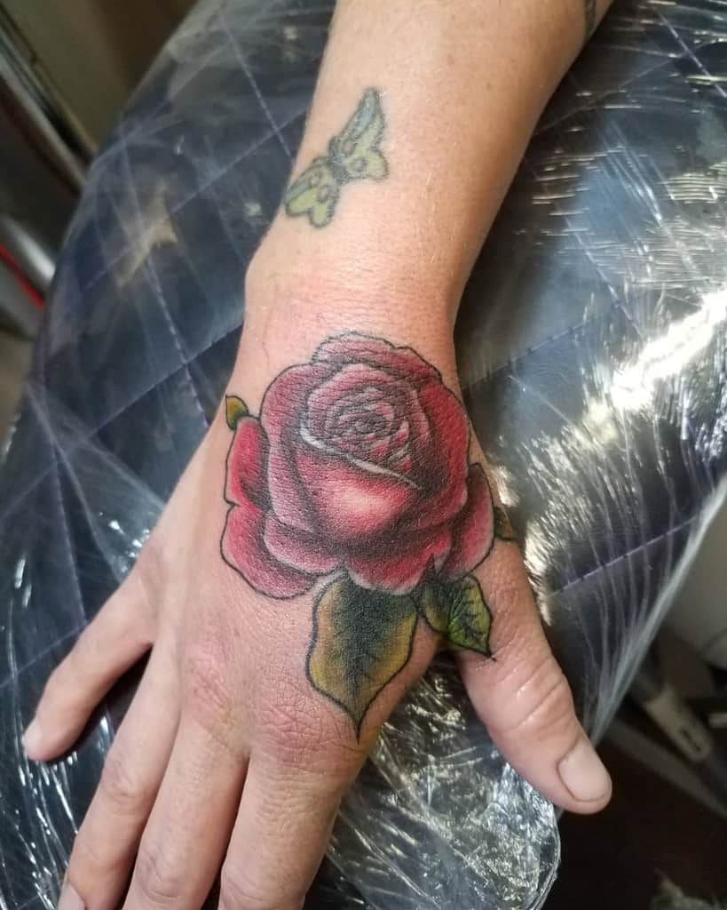 A hand tattoo features a striking red rose with verdant green leaves