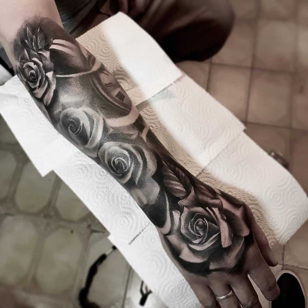 A stunning black and grey tattoo sleeve featuring intricate rose designs elegantly wraps around a person's forearm and hand