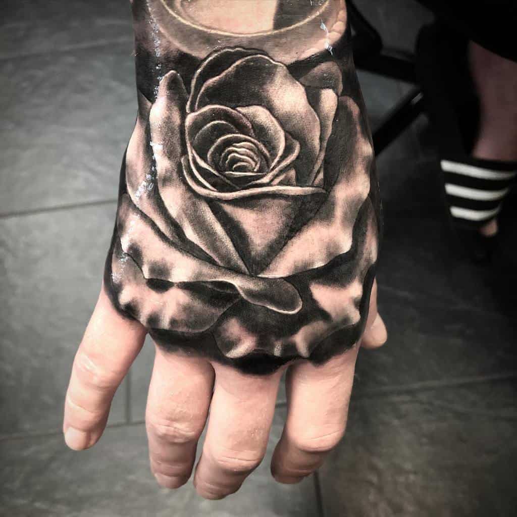 A stunning black and gray tattoo of a rose elegantly adorns the back of a hand
