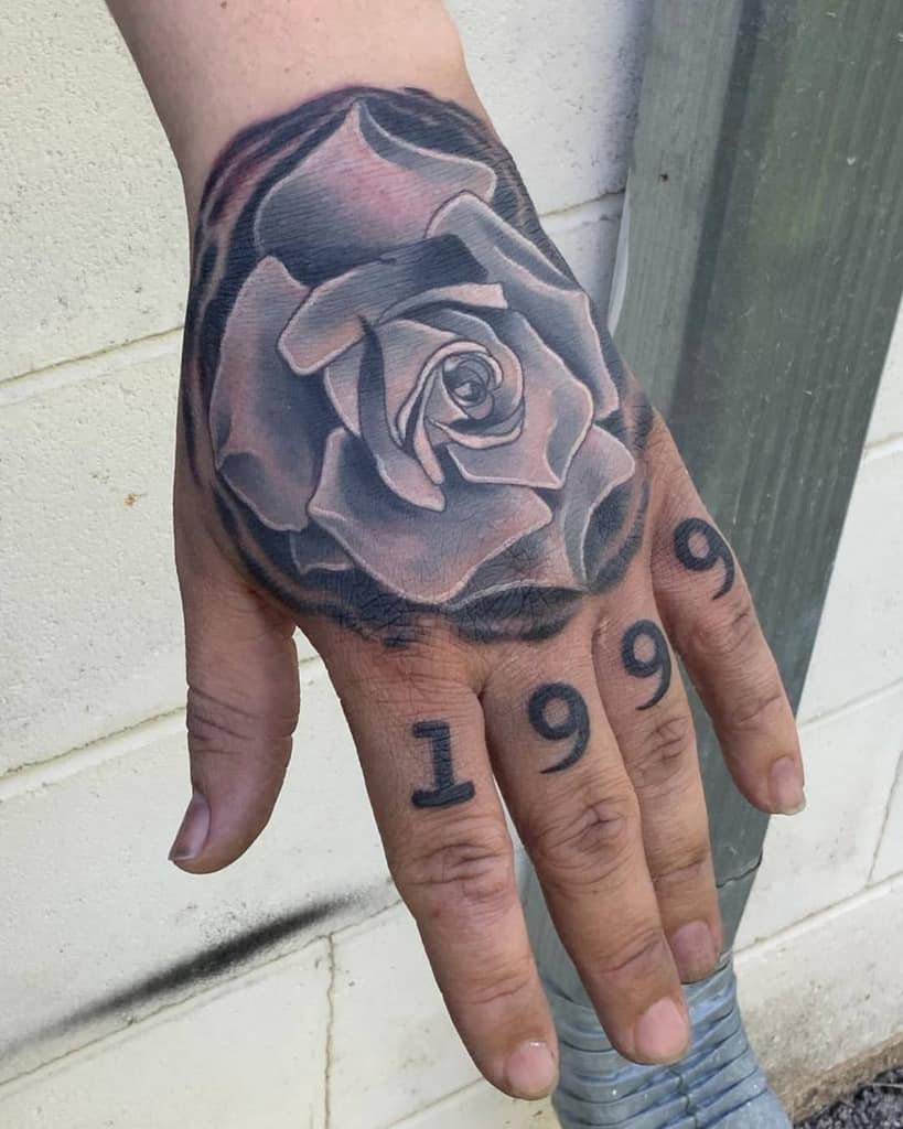 A hand with an intricate rose tattoo graces the skin, elegantly intertwined with the year "1999" inked across the fingers