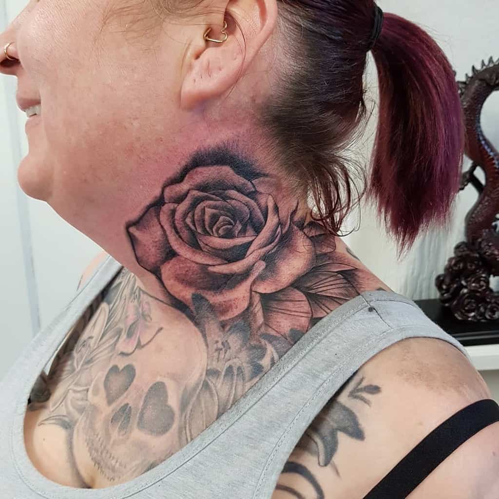Detailed black and grey rose tattoo on the side of the neck, featuring bold petals, fine shading, and leaf accents extending downward