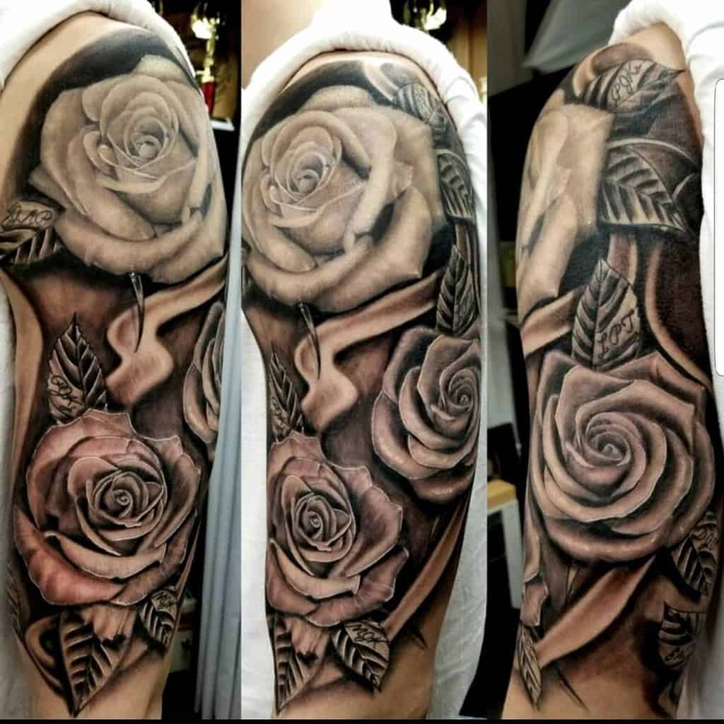 A detailed full sleeve tattoo featuring realistic black and gray roses with flowing ribbons and shading, adding depth and dimension to the intricate design