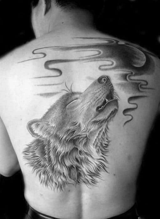 Detailed back tattoo of a wolf howling at the moon with swirling clouds