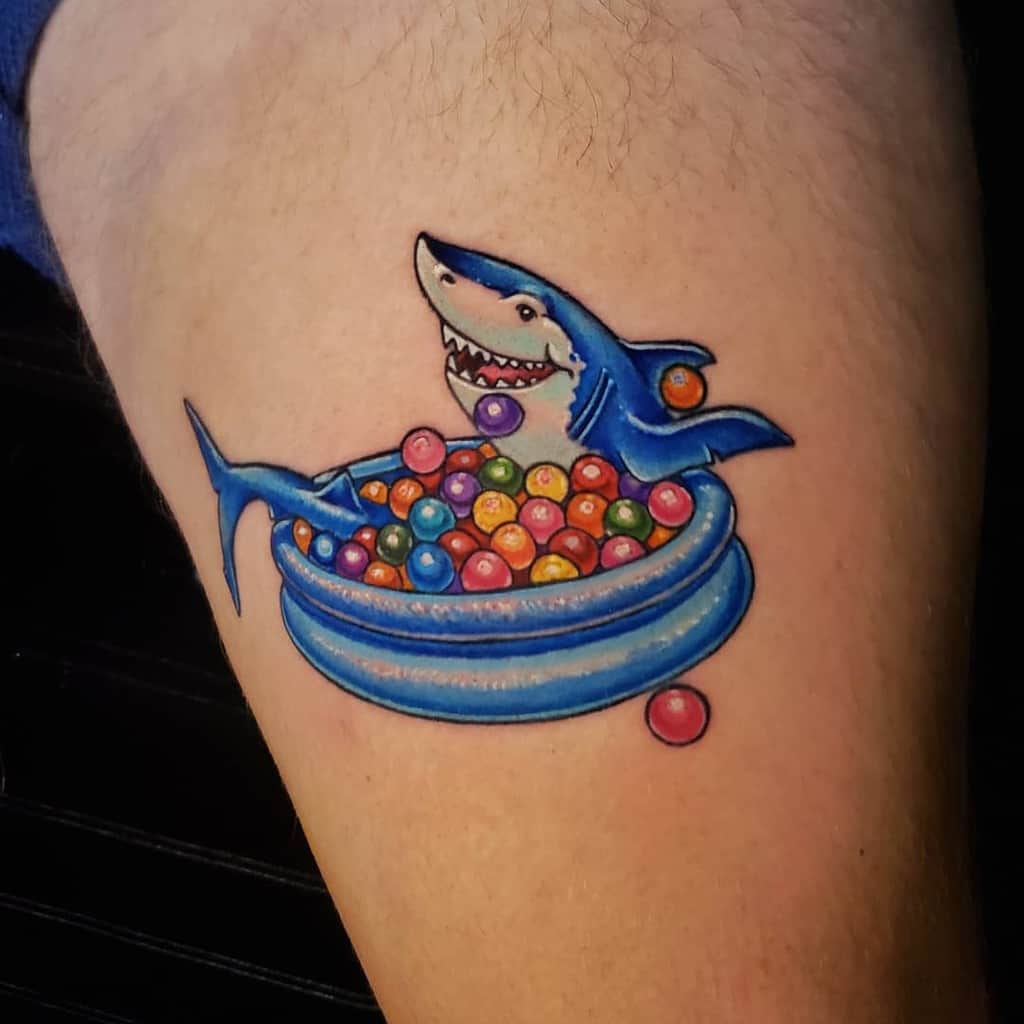 A colorful tattoo of a playful shark lounging in a ball pit, blending vibrant hues and cartoonish style for a fun and whimsical design.