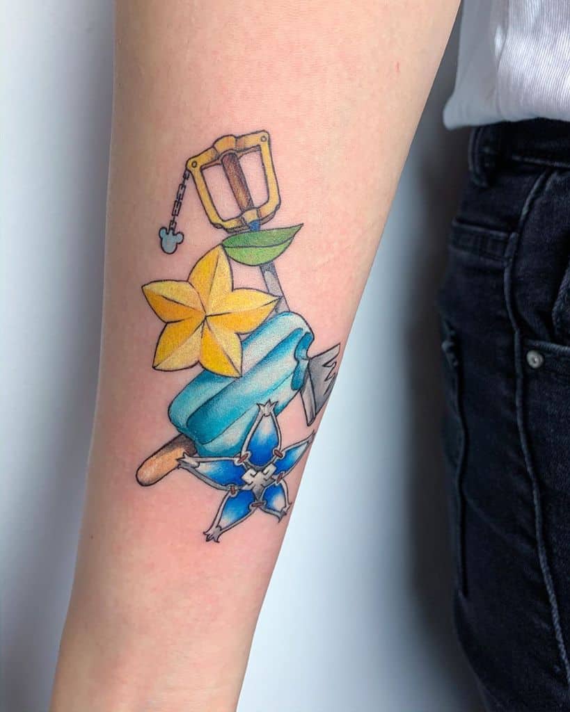 Colorful Kingdom Hearts tattoo featuring a Keyblade, Paopu fruit, sea-salt ice cream, and Wayfinder charm, symbolizing friendship.
