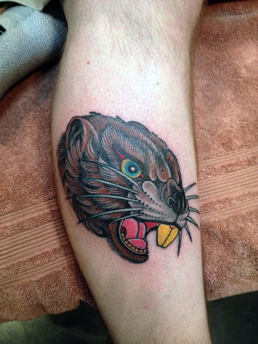 Traditional-style beaver head tattoo with fierce expression, bold outlines, exposed teeth, and striking teal eye on the calf.