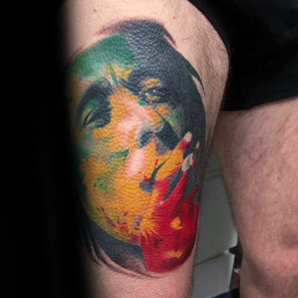 Colorful thigh tattoo of Bob Marley smoking, with abstract red, yellow, and green hues blending into his face in a bold, modern design.