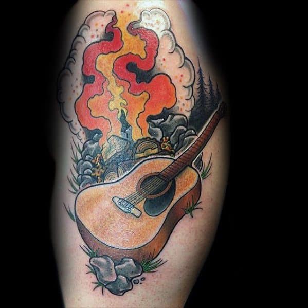 Colorful campfire tattoo with bright flames, smoke, rocks, and an acoustic guitar leaning on the ground, evoking a musical campsite vibe.