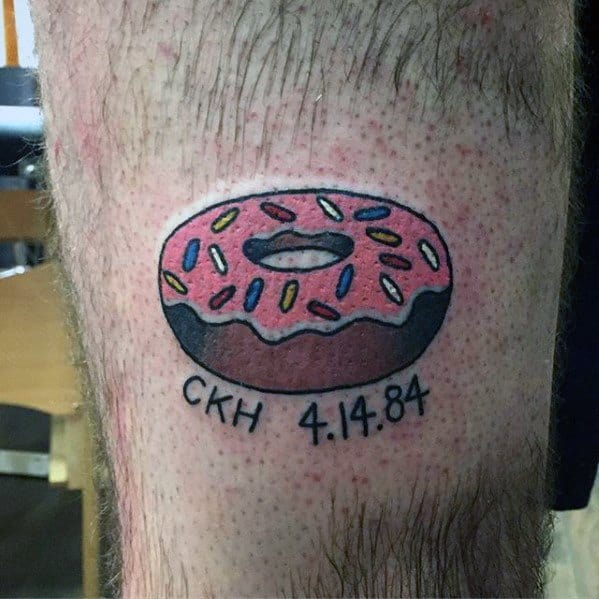 Tattoo of a pink frosted donut with colorful sprinkles, with the initials CKH and the date 4.14.84 written below as a personal tribute.