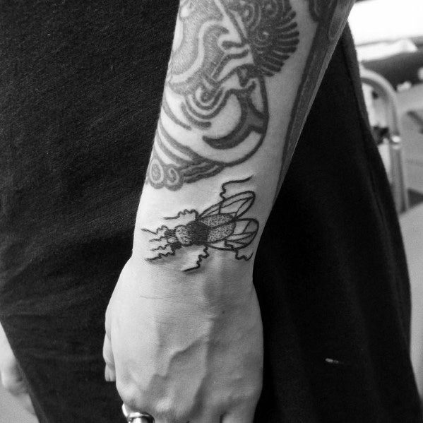 Blackwork fly tattoo on the wrist with bold lines, detailed wings, and jagged leg design, adding a striking touch to a sleeve composition.