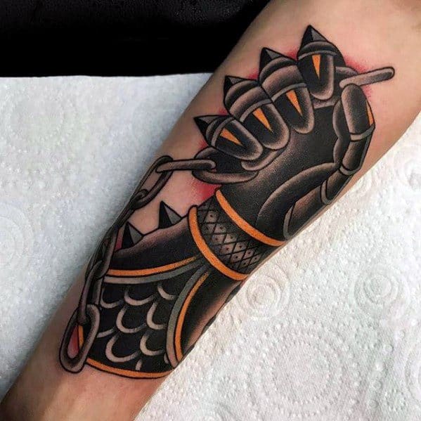 Bold tattoo of a black and gold armored gauntlet gripping a chain, featuring scale-like patterns and sharp clawed fingers.