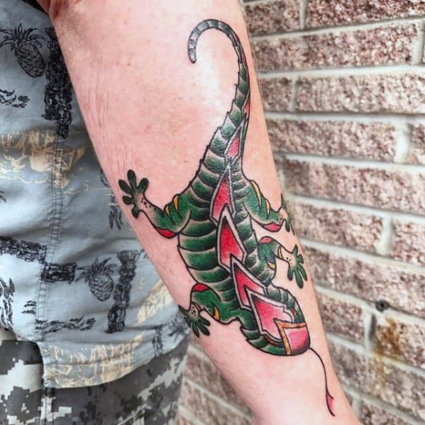 Colorful gecko tattoo on forearm with bold green and red scales, zigzag patterns, and thick black outlines for a striking look.