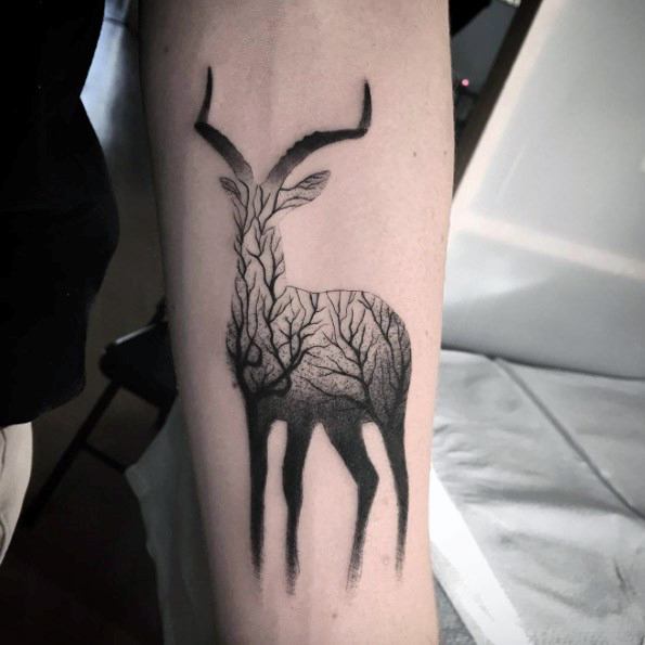 Black and grey gradient tattoo of an antelope silhouette filled with intricate tree branches, blending nature and wildlife into one design.