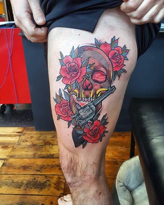 Colorful thigh tattoo of a cracked skull with glowing eyes, surrounded by red roses and a revolver, blending danger and beauty.
