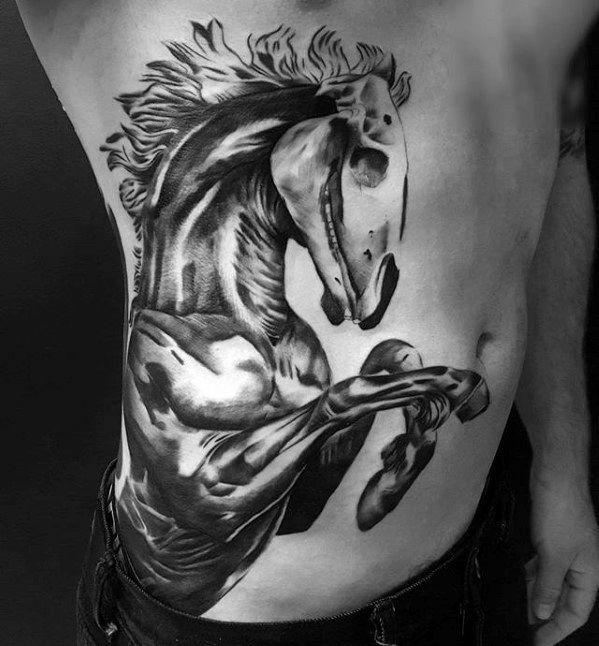 Large black and grey side tattoo of a powerful rearing horse with intense muscle detail and flowing mane across the ribs and torso