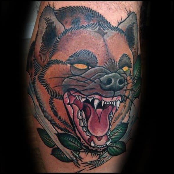 Bold neo-traditional hyena tattoo with glowing yellow eyes, open mouth and sharp teeth, surrounded by green leaves and white bone elements.