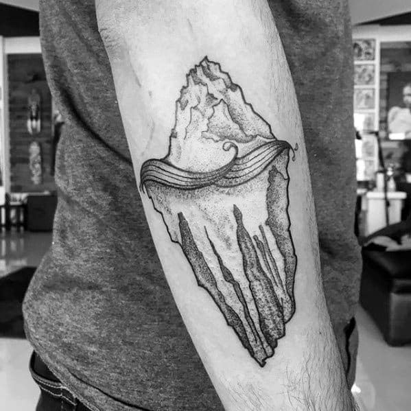 Dotwork iceberg tattoo on the forearm with flowing wave detail at the waterline and jagged textures emphasizing depth below.
