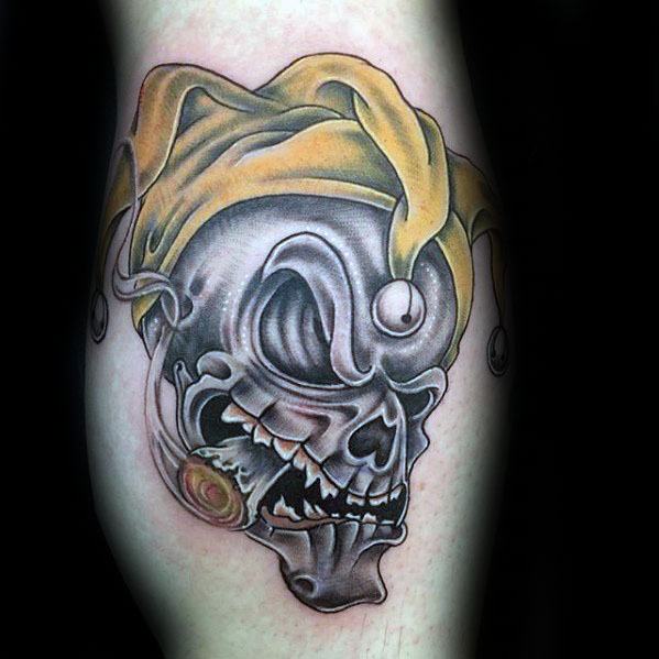 A colorful tattoo of a skull wearing a yellow jester hat, featuring bold shading and vivid details, placed on the forearm.