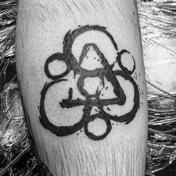 Bold black Coheed and Cambria Keywork tattoo on the calf, featuring thick brushstroke lines and scattered ink splatter detailing.