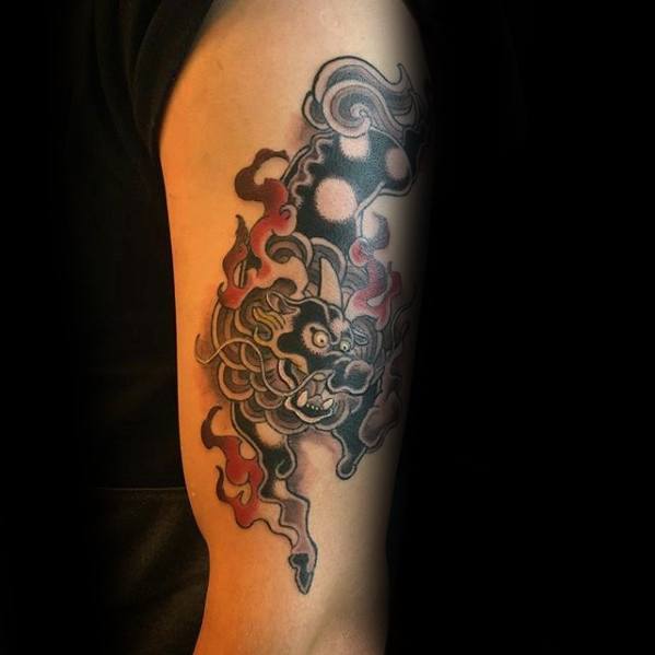 Bold Kirin tattoo on upper arm with dark tones, red flames, and swirling black clouds, showcasing a fierce expression in traditional style.
