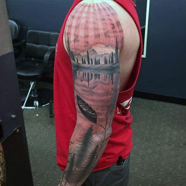 Full arm tattoo with a surreal red-toned lake scene, mirrored forest and mountains, a canoe, and beams of light radiating from above.