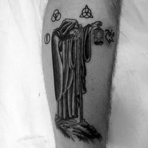Leg tattoo of Led Zeppelin’s hermit holding a lantern on a cliff, with the four band symbols—Zoso, triquetra, Borromean rings, and feather—above.