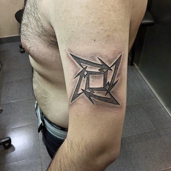 Upper arm tattoo of the classic Metallica ninja star logo in black and grey, featuring sharp edges and a bold 3D effect.