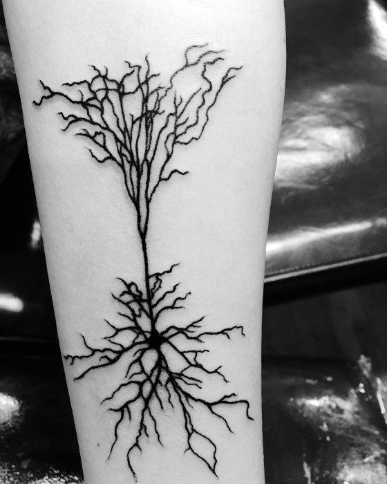Minimalist black ink neuron tattoo on forearm with a central cell body and thin, tree-like dendrites branching up and down.