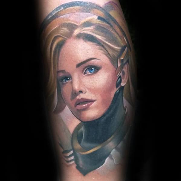 Realistic portrait tattoo of Mercy from Overwatch, highlighting her blonde hair, glowing blue eyes, and signature headset.