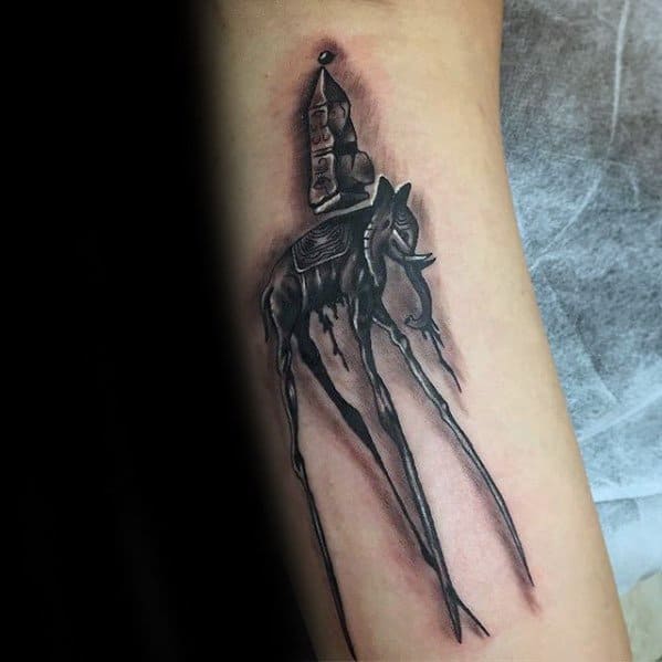 Black and grey Salvador Dali-style tattoo of a surreal elephant with elongated legs and a towering obelisk, surrounded by soft shading.