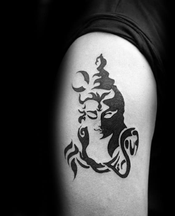 Bold black ink tattoo of Lord Shiva with abstract strokes, featuring the crescent moon, serpent, and Om symbol on the upper arm.