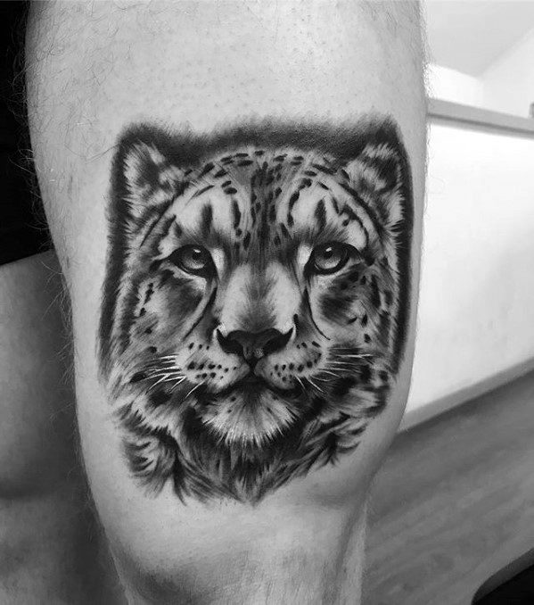 Realistic snow leopard tattoo in black and gray on the thigh, showcasing soft shading, lifelike fur, and a calm, focused gaze.