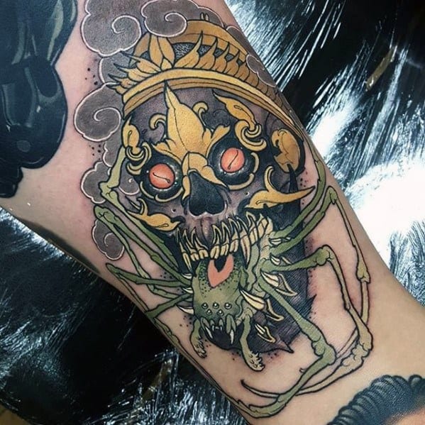Tibetan skull tattoo with glowing red eyes, golden crown, and a large menacing spider crawling over the face, set against smoky clouds.