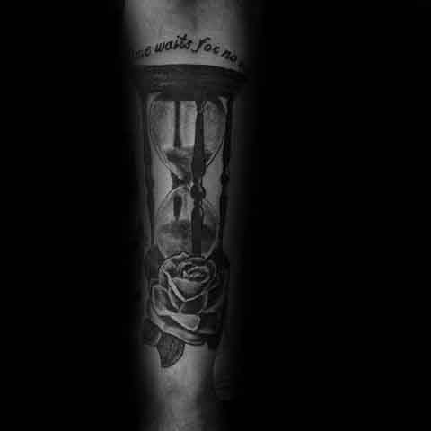 Black and grey tattoo of an hourglass with sand and a rose beneath, featuring the phrase Time Waits for No One above.