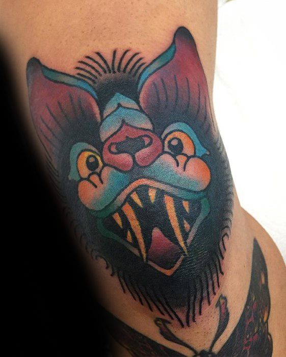 Vibrant traditional bat head tattoo with bold teal, purple, and orange tones, sharp fangs, and exaggerated expression.