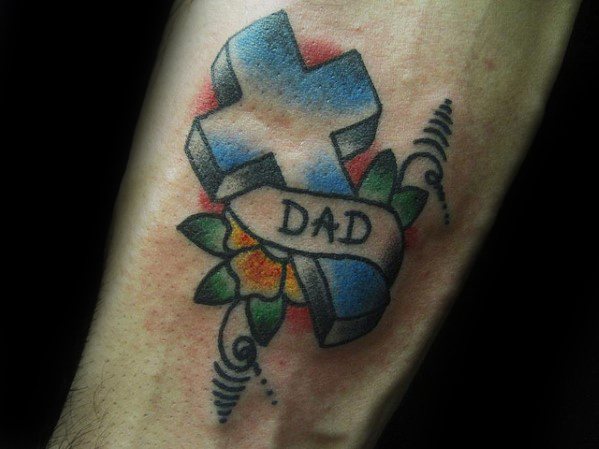 Blue 3D cross tattoo with a banner reading "DAD," surrounded by a yellow flower, green leaves, and red shading in a traditional style.