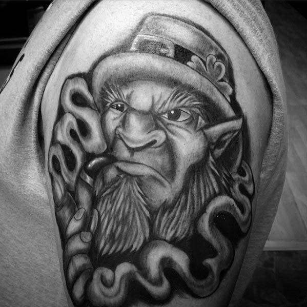 Black and grey tattoo of a stern-faced leprechaun with pointed ears, smoking a pipe, surrounded by swirling smoke and a shamrock hat.