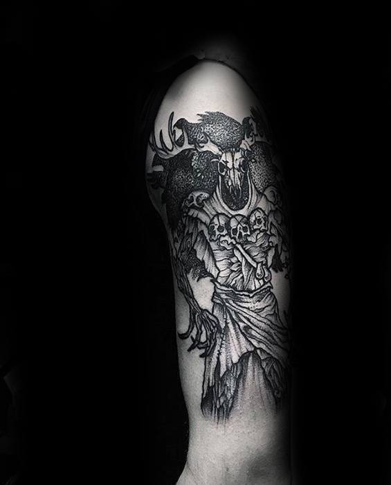 Dark fantasy Witcher tattoo on the upper arm featuring a Leshen with a skull face, antlers, ravens, and a cloak of bones and tattered fabric.