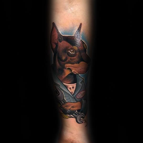 Color tattoo of a Doberman in a mechanic uniform holding a wrench, blending realism and cartoon style for a bold, character-driven design.