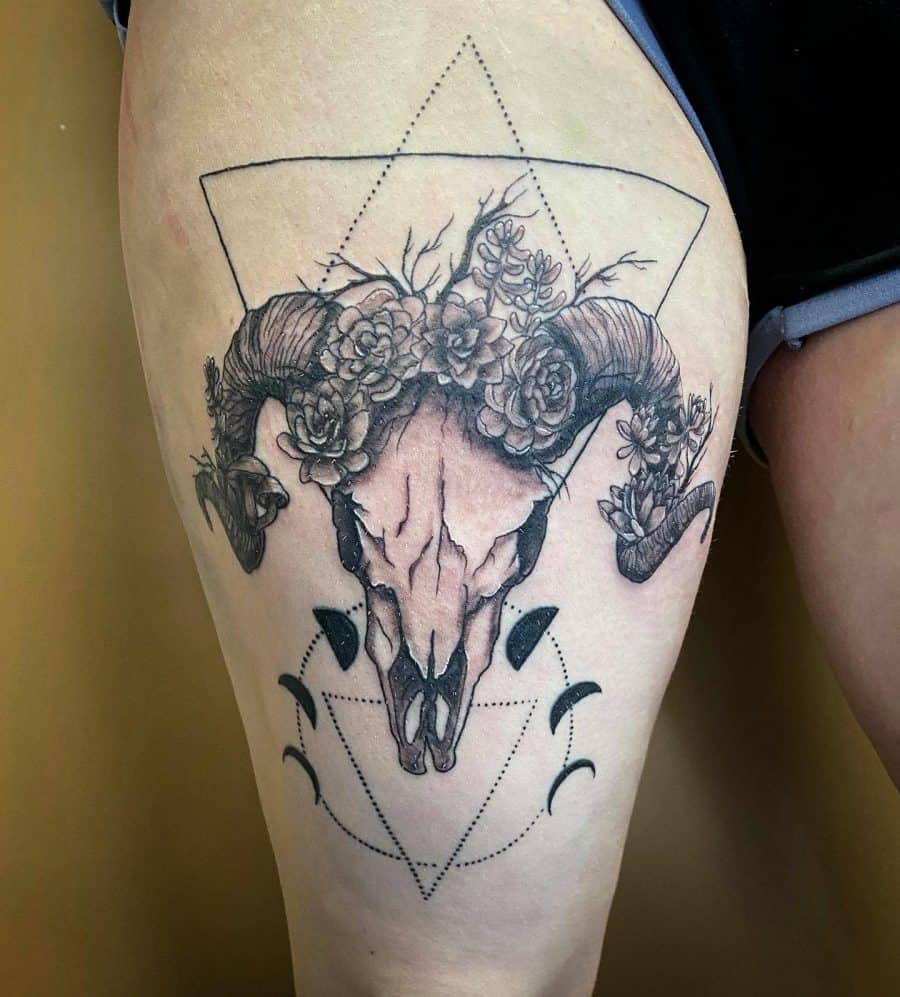 Thigh tattoo of a ram skull adorned with flowers and geometric shapes, blending nature, symbolism, and fine linework for a striking design.