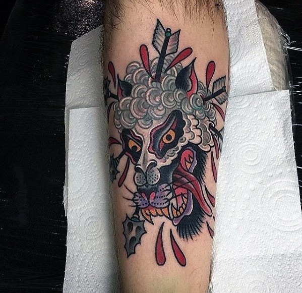 Tattoo of a snarling wolf's head with arrows and red accents on forearm