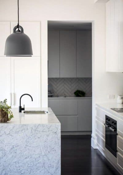 Modern kitchen with marble island, black pendant light, and hidden pantry shelving.