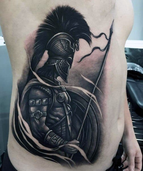 Large side torso tattoo of a Spartan warrior in profile, featuring a crested helmet, spear, shield, and dynamic shading for a bold, powerful look.