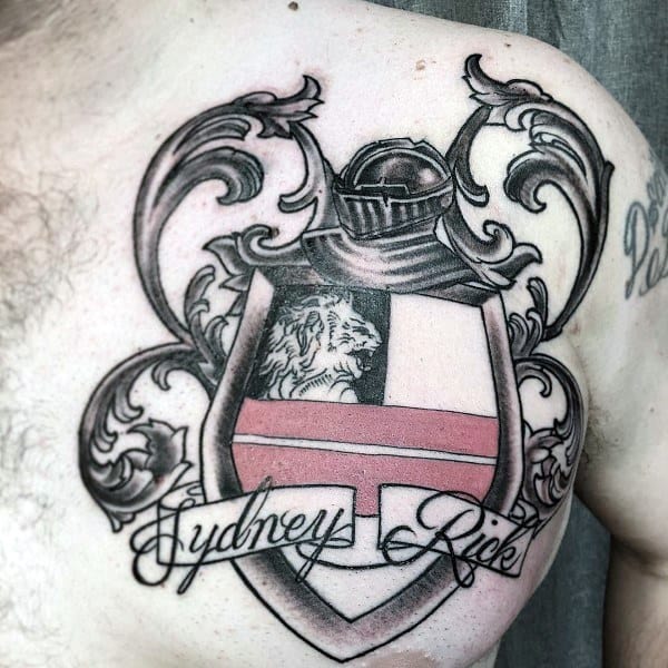 Upper chest tattoo of a family crest featuring a lion, knight’s helmet, red cross, ornate scrollwork, and the names “Sydney” and “Rick” in script.