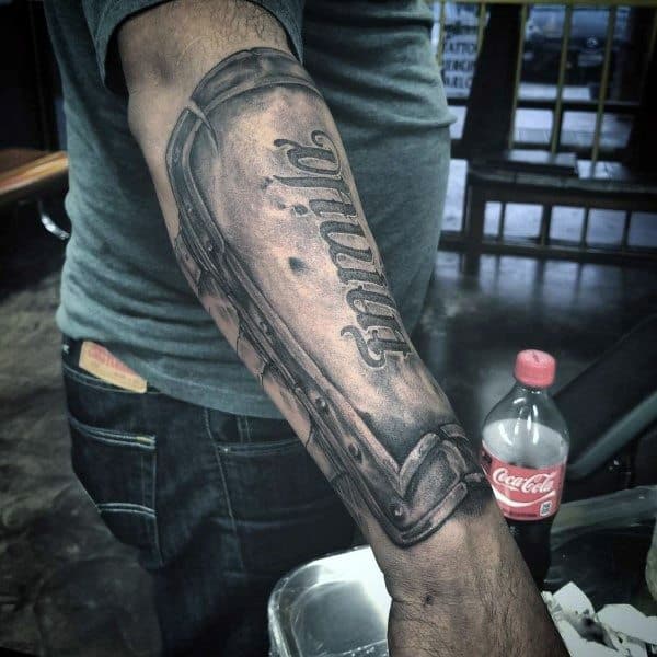 Realistic forearm tattoo of a medieval-style shield with the word *faith* engraved, designed to look like armor plating.