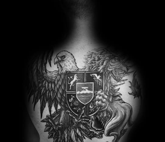 Detailed upper back tattoo of an eagle and lion holding a divided shield with various emblems, symbolizing strength, balance, and heraldic power.