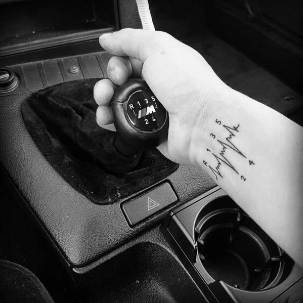 BMW M gear shift tattoo on wrist, featuring a heartbeat line integrated with the manual transmission pattern for a passionate driving design.